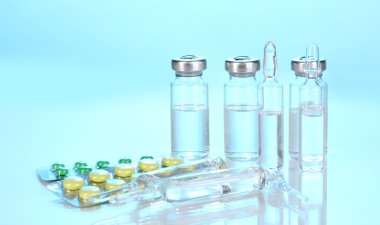 Syringe with medical ampoules and tablets on blue background clipart
