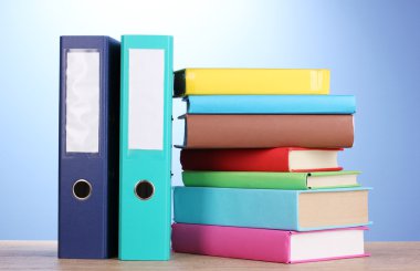 Bright office folders and books on wooden table on blue background clipart