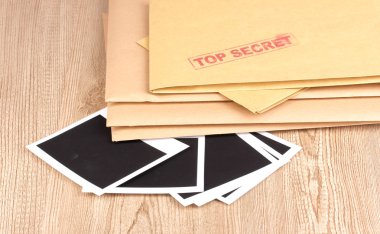 Envelopes with top secret stamp with photo papers close-up on wooden background clipart