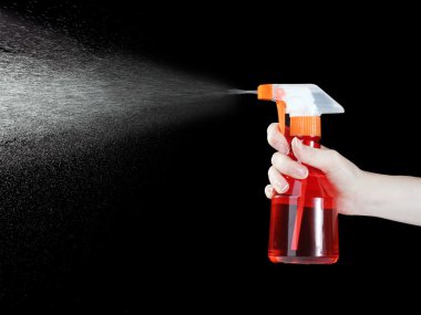 Hand holding spray bottle and spraying on black background clipart