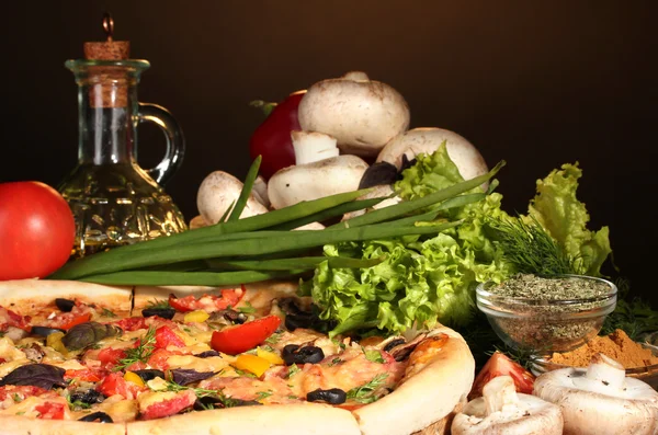 Délicieuse pizza, légumes et épices sur table en bois sur fond marron — Photo