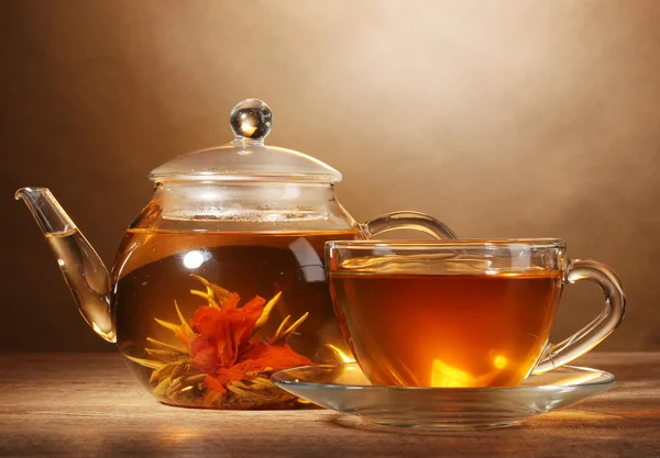 Szklany czajnik i filiżanki z egzotycznych zielonej herbaty na drewnianym stole na brązowym tle — Zdjęcie stockowe