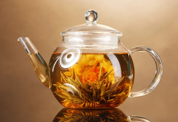 Glas theepot met exotische groene thee op houten tafel op bruine achtergrond — Stockfoto