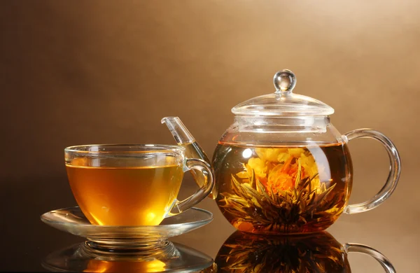 Szklany czajnik i filiżanki z egzotycznych zielonej herbaty na drewnianym stole na brązowym tle — Zdjęcie stockowe