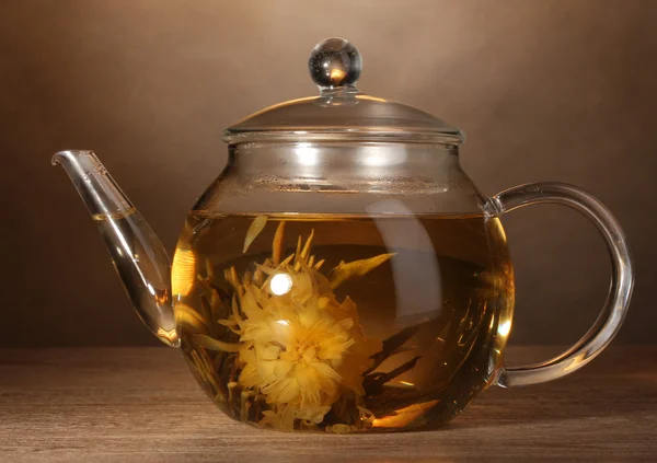 Théière en verre avec thé vert exotique sur table en bois sur fond brun — Photo