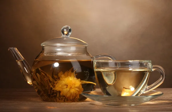 Teiera di vetro e tazza con tè verde esotico su tavolo di legno su sfondo marrone — Foto Stock