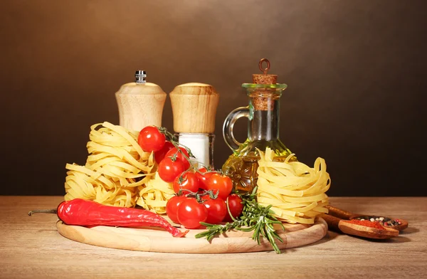 Лапша в миске, банка масла, специи и овощи на деревянном столе на коричневом фоне — стоковое фото