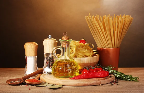 Spagetti, nuudelit kulhossa, purkki öljyä ja vihanneksia puupöydällä ruskealla pohjalla — kuvapankkivalokuva