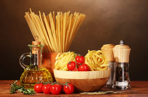 Spaghetti, tagliatelle in ciotola, vasetto di olio e verdure su tavola di legno su fondo marrone — Foto Stock