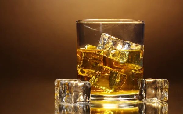 stock image Glass of whiskey and ice on brown background