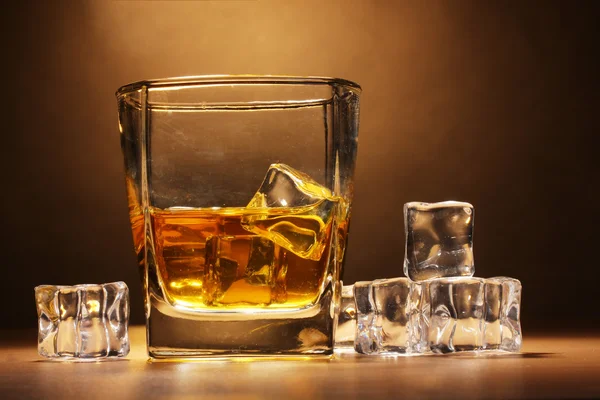 Stock image Glass of scotch whiskey and ice on wooden table on brown background