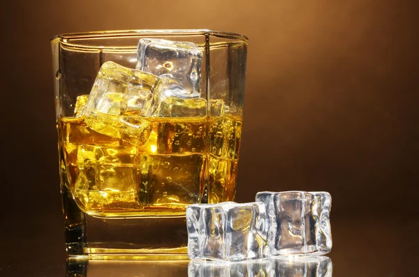 Стакан виски и лед на коричневом фоне — стоковое фото