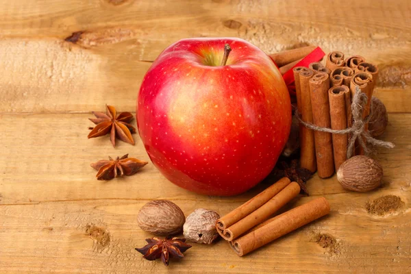Kaneelstokjes, rode appel, nootmuskaat en anijs op houten tafel — Stockfoto