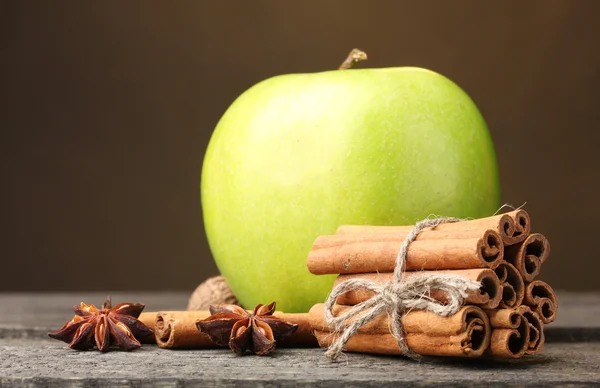 Bastoncini di cannella, mela verde e anice su tavolo di legno su sfondo marrone — Foto Stock