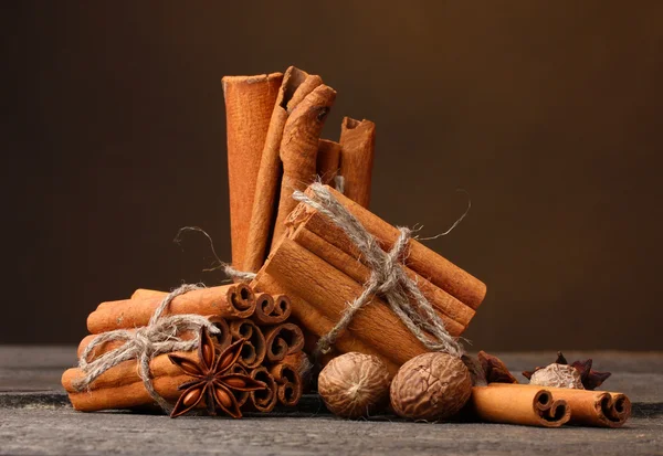 Палички кориці, мускатний горіх та аніс на дерев'яному столі на коричневому фоні — стокове фото
