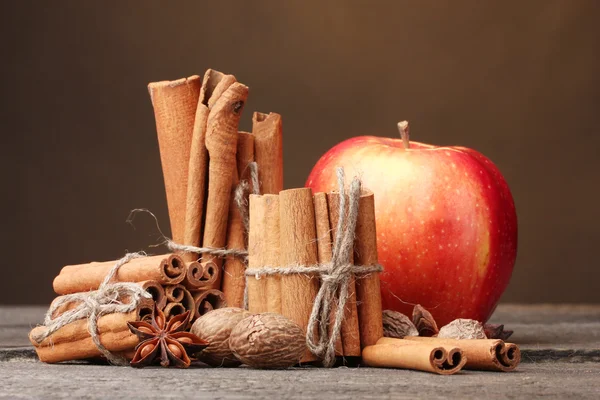 Bâtonnets de cannelle, pomme rouge, muscade et anis sur table en bois sur fond brun — Photo