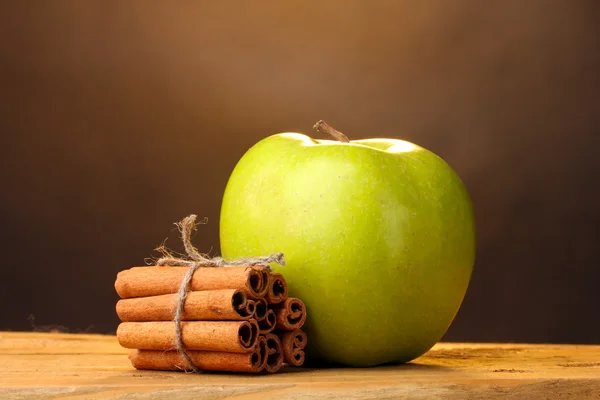 Bastoncini di cannella e mela verde su tavolo di legno su sfondo marrone — Foto Stock