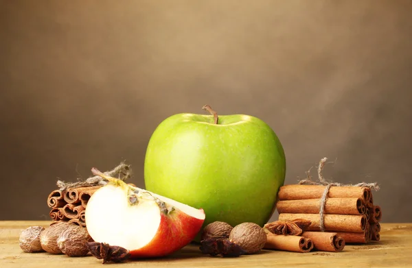 Tyčinky skořice, jablka, muškátový oříšek a anýzu na dřevěný stůl na hnědé pozadí — Stock fotografie