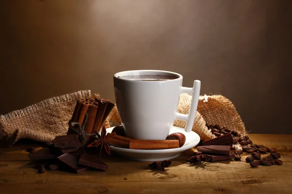 Φλιτζάνι ζεστή σοκολάτα, ξυλάκια κανέλας, καρύδια και σοκολάτα στο ξύλινο τραπέζι για καφέ φόντο — Φωτογραφία Αρχείου