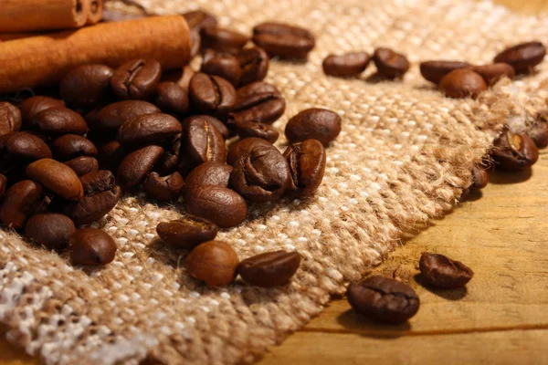 Grãos de café e paus de canela no saque na mesa de madeira — Fotografia de Stock
