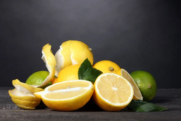 Mogna citroner och limefrukter med blad på träbord på grå bakgrund — Stockfoto