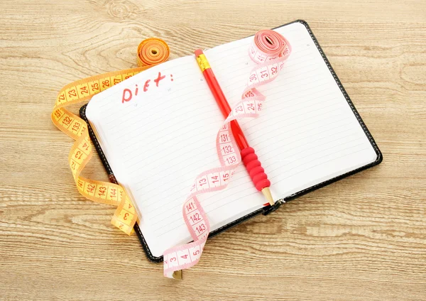 Pianificazione di dieta. Nastri di misurazione per notebook e penna su tavolo in legno — Foto Stock