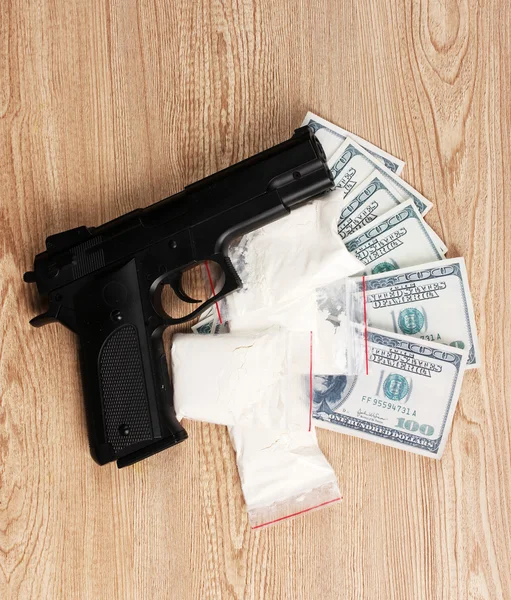 Cocaïne in pakketten, dollars en pistool op houten achtergrond — Stockfoto