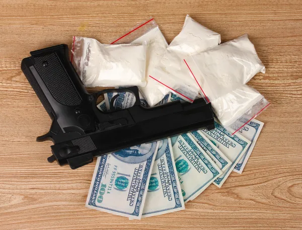 Cocaine in packages, dollars and handgun on wooden background — Stock Photo, Image
