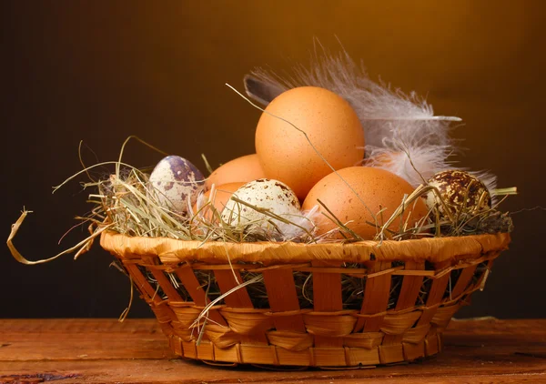 Kip en kwartel eieren in een nest op houten tafel op bruine achtergrond — Stockfoto