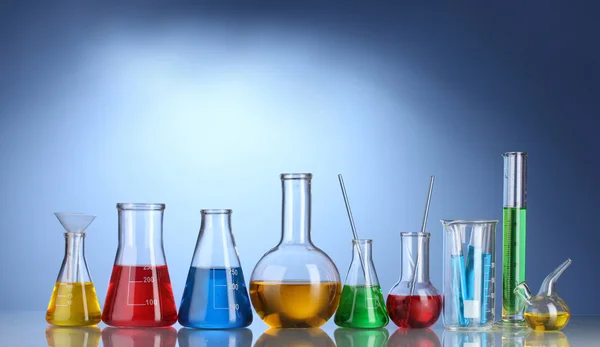 Különböző laboratóriumi üvegeszközök, színes folyadékkal és elmélkedés, a kék háttér — Stock Fotó