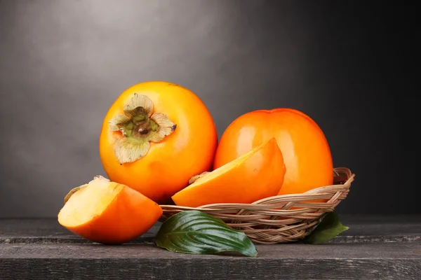 Appetizing persimmons in pad on wooden table on grey background — Stock Photo, Image