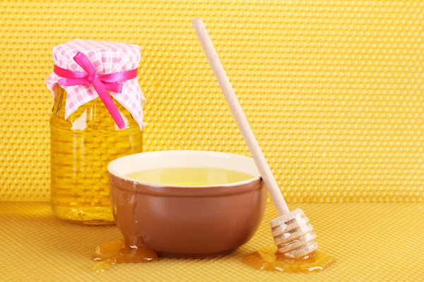 Jar of honey, bowl and wooden drizzler with honey on yellow honeycomb background — Stock Photo, Image