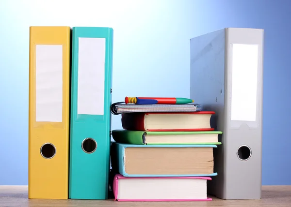 Jasne biuro folderów i książek z papeterii na drewnianym stole na niebieskim tle — Zdjęcie stockowe