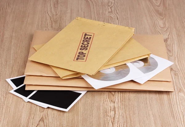 Envelopes com selo ultra-secreto com papéis fotográficos e discos de CD sobre fundo de madeira — Fotografia de Stock