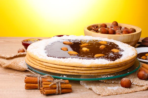 Cake on glass stand and nuts on wooden table on yellow background — Stock Photo, Image
