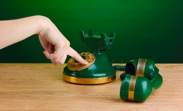 stock image Dialing on retro phone on wooden table on green background