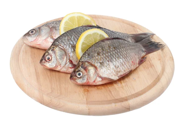 Fresh fishes with lemon on wooden cutting board isolated on white — Stock Photo, Image