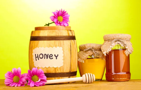 Dolce miele in botte e vasetti con drizzler su tavolo in legno su fondo verde — Foto Stock