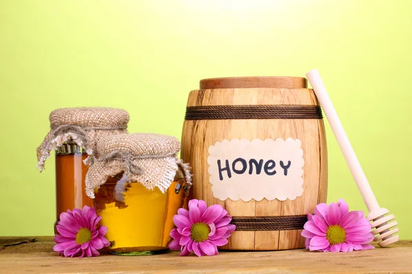 Miel dulce en barril y frascos con rociador sobre mesa de madera sobre fondo verde —  Fotos de Stock