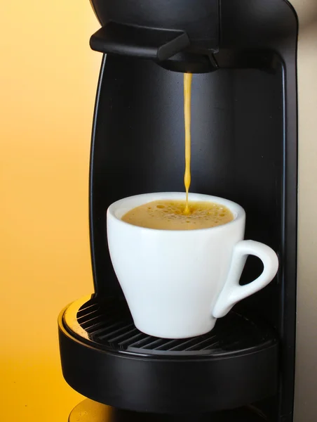 Ekspres do kawy nalewający kawę do filiżanki na brązowym tle — Zdjęcie stockowe