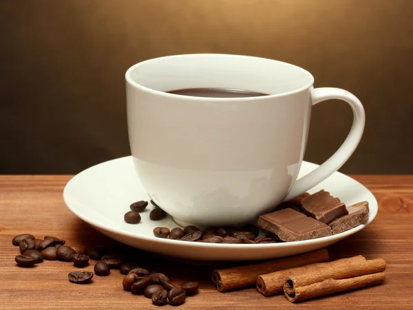 コーヒー、豆、シナモンスティック、チョコレート茶色の背景に木製のテーブルの上のカップ — ストック写真