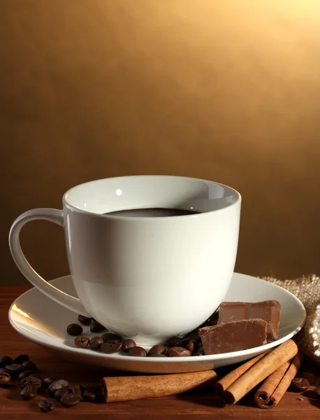 Taza de café y frijoles, palitos de canela y chocolate sobre mesa de madera sobre fondo marrón — Foto de Stock