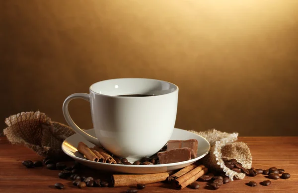Kopp kaffe och bönor, kanelstänger och choklad på träbord på brun bakgrund — Stockfoto