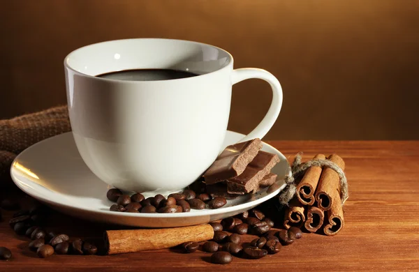 Tazza di caffè e fagioli, bastoncini di cannella e cioccolato su tavolo di legno su sfondo marrone — Foto Stock