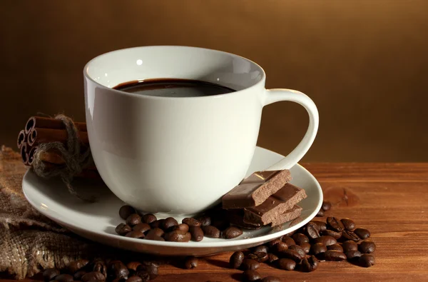 Tasse Kaffee, Bohnen und Schokolade auf Holztisch auf braunem Hintergrund — Stockfoto