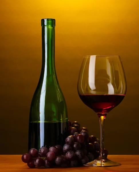 Composition of wine bottle and wineglass on wooden table on brown background — Stock Photo, Image