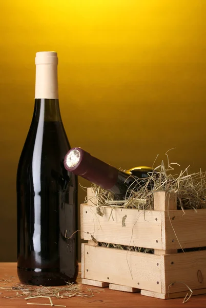 Láhev značkového vína v bedně na dřevěný stůl na hnědé pozadí — Stock fotografie