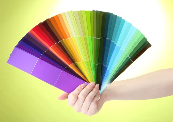 Hand som håller ljusa palett av färger på grön bakgrund — Stockfoto