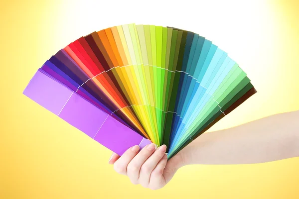 Hand som håller ljusa palett av färger på gul bakgrund — Stockfoto