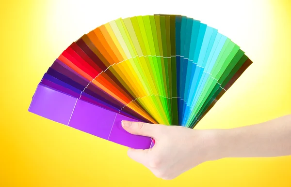 Hand holding bright palette of colors on yellow background — Stock Photo, Image